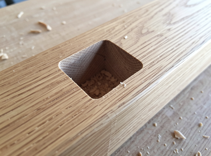 A square-bottomed mortise pocket freshly cut by a CNC router into an oak rail