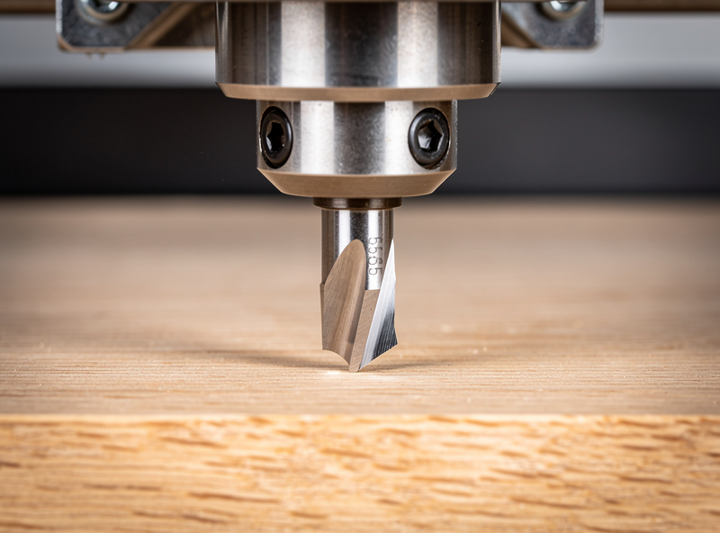 A 60 degree V-bit loaded in a desktop CNC spindle above a hardwood sign blank
