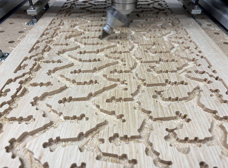 Several tiny wood parts being machined on a CNC while held down with double-sided tape on a spoilboard